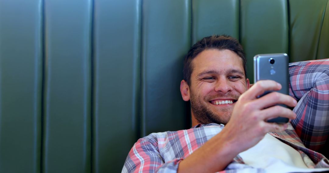 Smiling Man Holding Smartphone Relaxing on Green Sofa - Free Images, Stock Photos and Pictures on Pikwizard.com