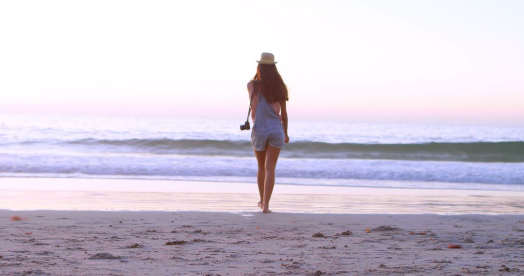 Woman Walking Into Serene Beach Sunset with Camera - Free Images, Stock Photos and Pictures on Pikwizard.com