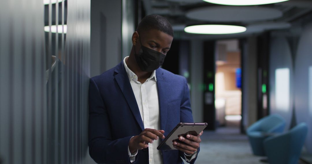 Businessman Using Tablet in Modern Office Corridor with Face Mask - Free Images, Stock Photos and Pictures on Pikwizard.com