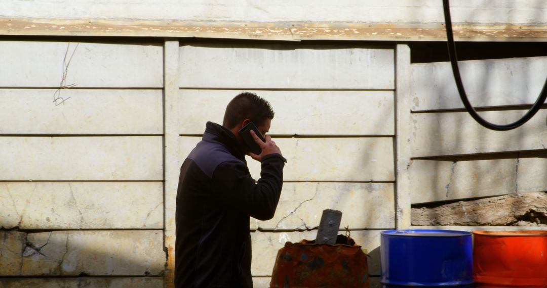 Man Talking on Phone Next to Metal Barrels in Industrial Area - Free Images, Stock Photos and Pictures on Pikwizard.com