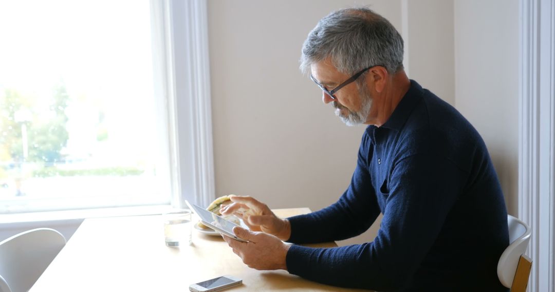 Mature Man Reading Digital Tablet While Eating Breakfast - Free Images, Stock Photos and Pictures on Pikwizard.com