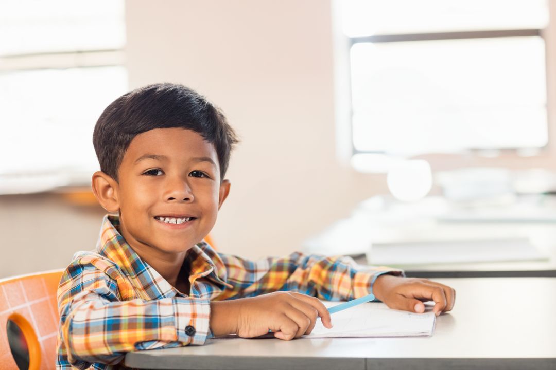 Smiling Young Boy Engaged in Classroom Activities at Desk