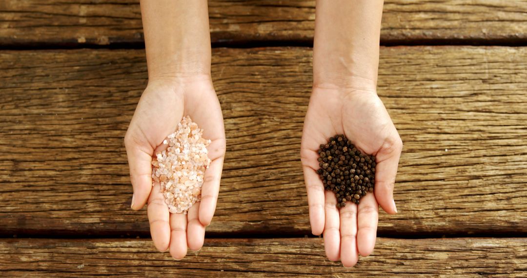 Hands Presenting Pink Salt and Black Peppercorns on Wooden Background - Free Images, Stock Photos and Pictures on Pikwizard.com