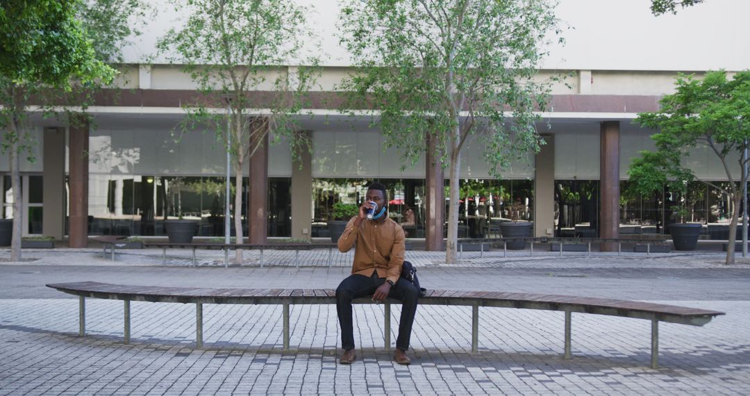 Man sitting on bench and drinking coffee in modern urban plaza - Free Images, Stock Photos and Pictures on Pikwizard.com