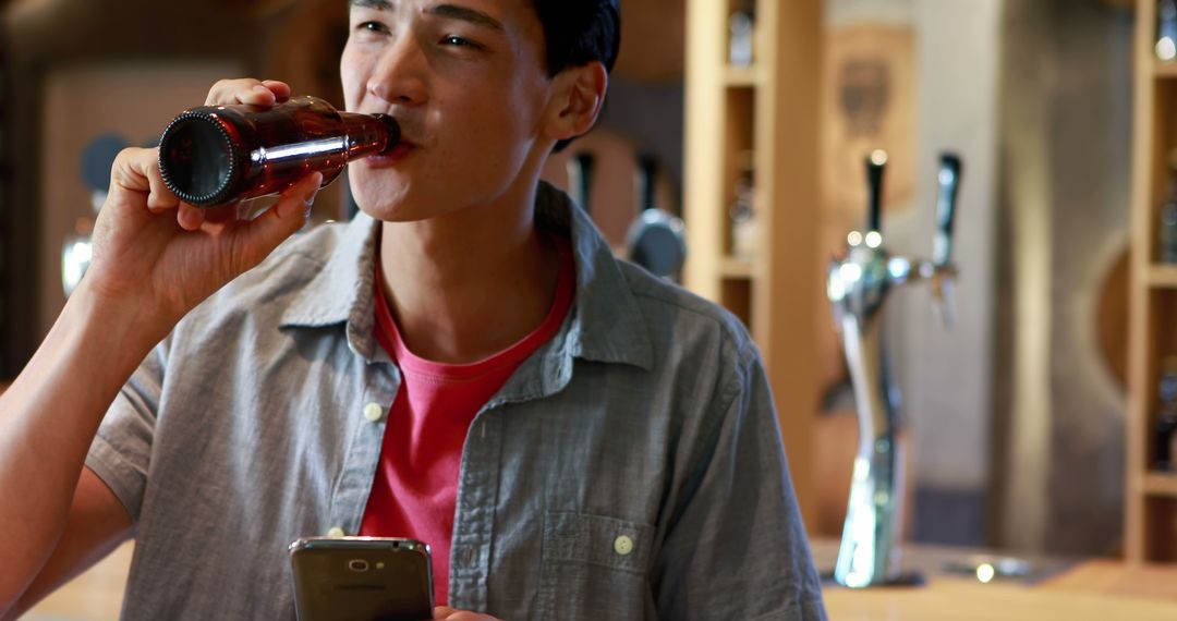 Young man enjoying drink while using smartphone in casual café