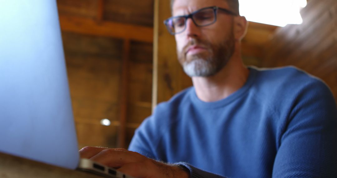 Focused Mature Man in Glasses Working on Laptop in Rustic Workspace - Free Images, Stock Photos and Pictures on Pikwizard.com