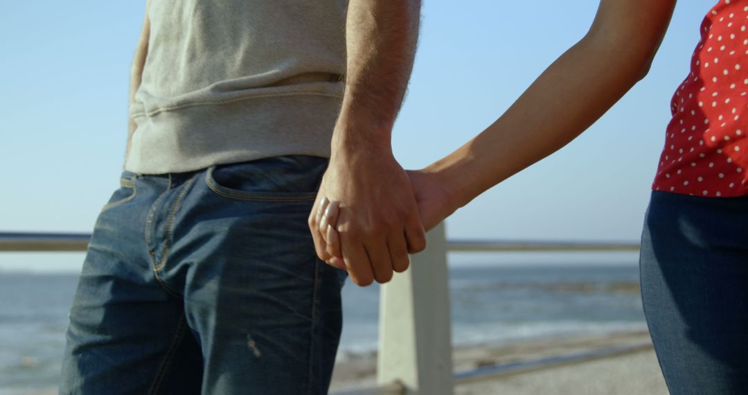 A diverse couple is holding hands by sea, enjoying sunny day - Free Images, Stock Photos and Pictures on Pikwizard.com