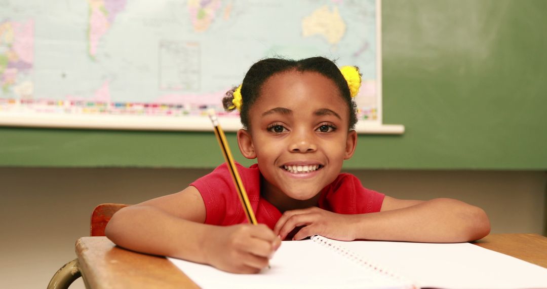 Smiling Schoolgirl Writing in Classroom with World Map Background