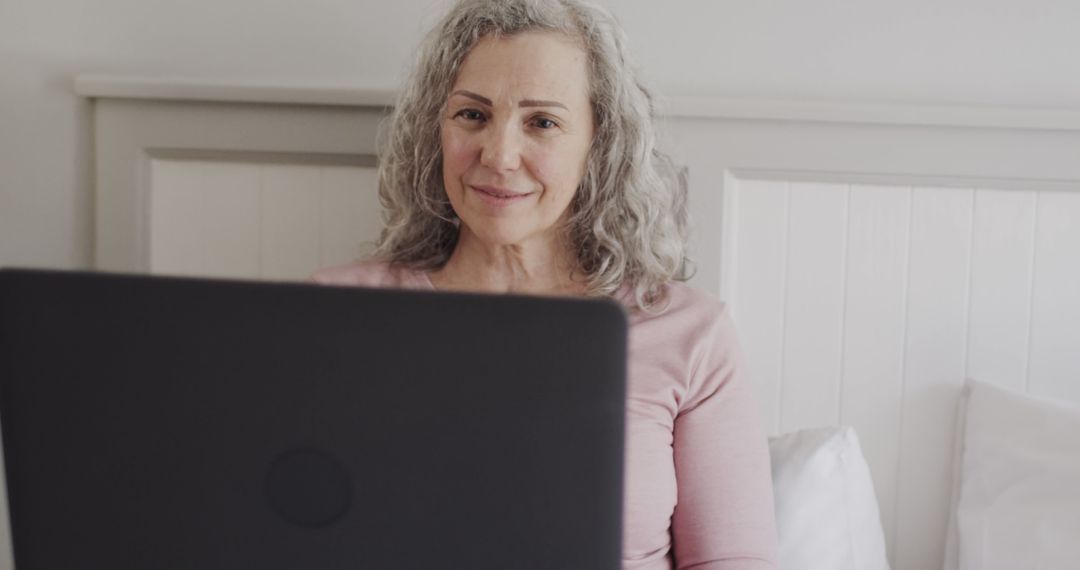 Senior woman with laptop in bed smiling confidently - Free Images, Stock Photos and Pictures on Pikwizard.com