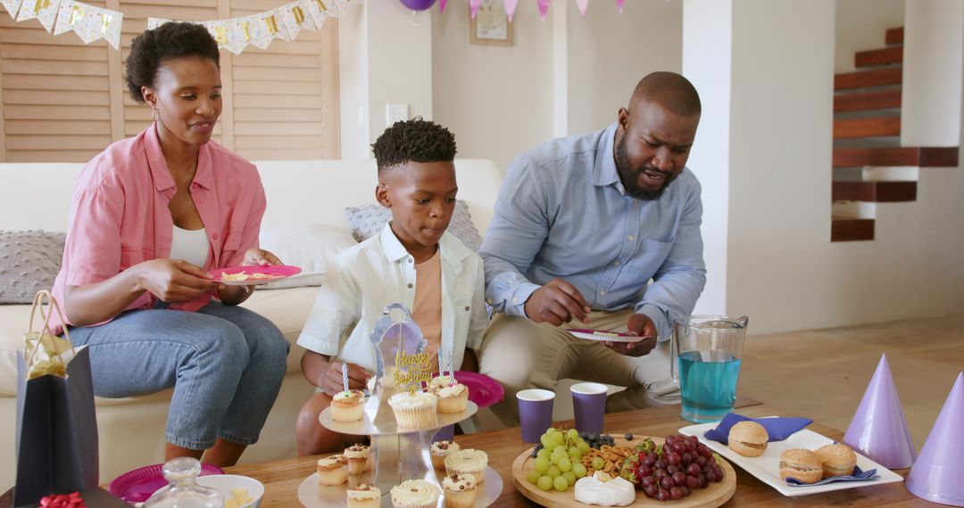 Family celebrating son's birthday at home with cupcakes, snacks and colorful party decorations