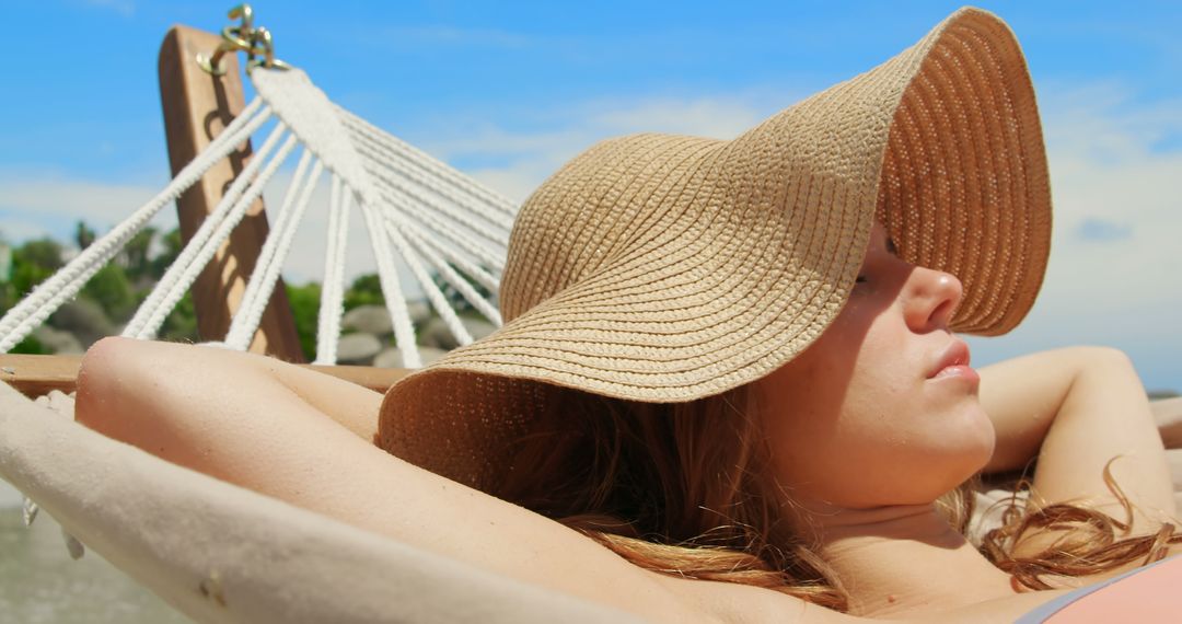 Woman Relaxing in Hammock Under Straw Hat on Beach