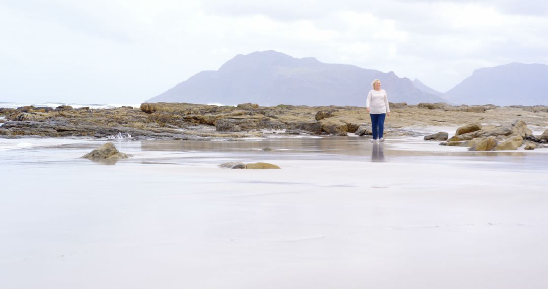 Elderly Woman Enjoying Peaceful Walk on Serene Rocky Beach - Free Images, Stock Photos and Pictures on Pikwizard.com