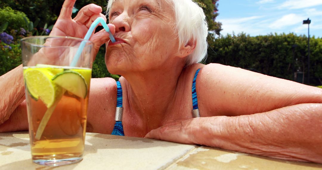 Elderly Woman Enjoying Refreshing Drink by Poolside on Sunny Day - Free Images, Stock Photos and Pictures on Pikwizard.com