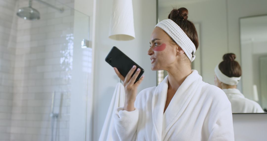 Woman in Bathrobe Calls with Under Eye Patches in Modern Bathroom