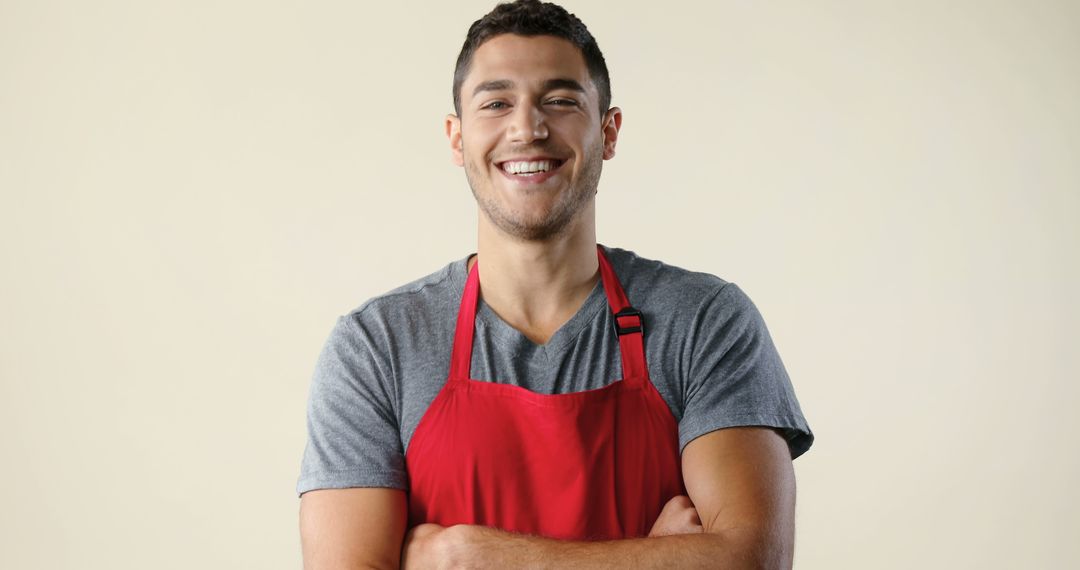 Young smiling man wearing red apron on beige background - Free Images, Stock Photos and Pictures on Pikwizard.com