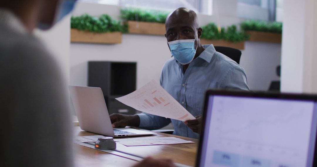 Masked Businessman Analyzing Financial Documents in Office - Free Images, Stock Photos and Pictures on Pikwizard.com