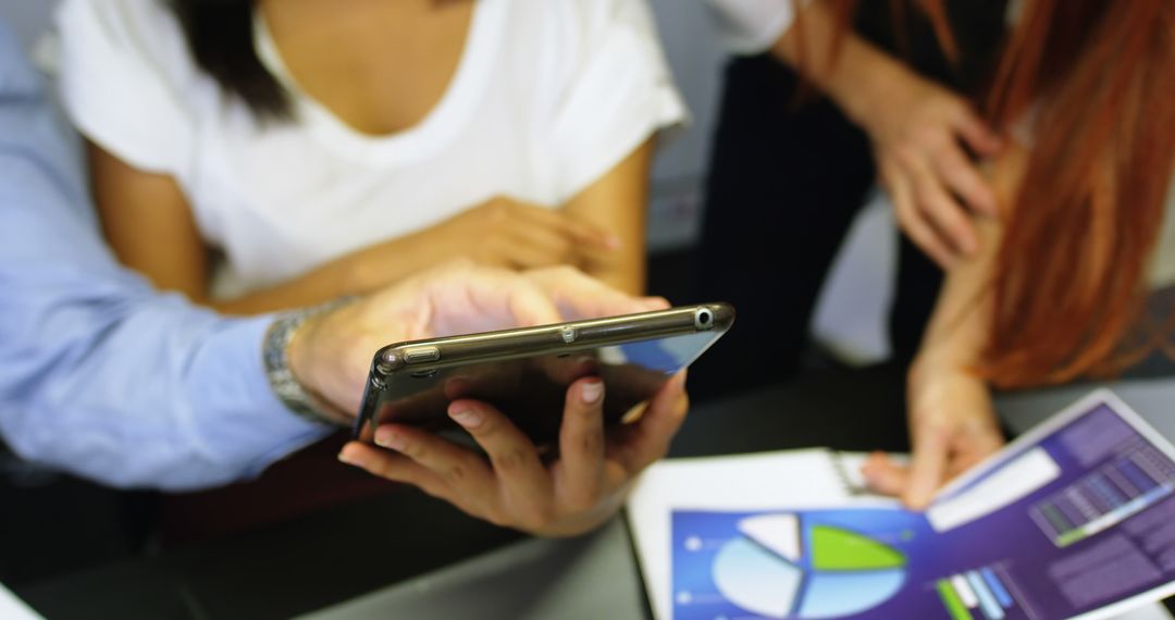 Colleagues Collaborating in Office with Smartphone and Printed Charts