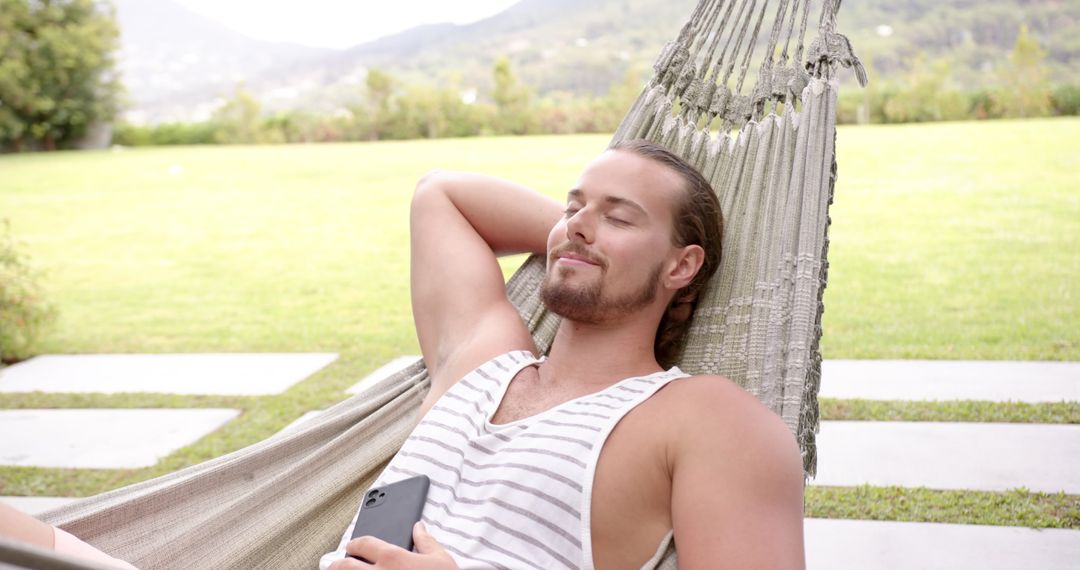Young Man Relaxing in Hammock with Smartphone in Backyard