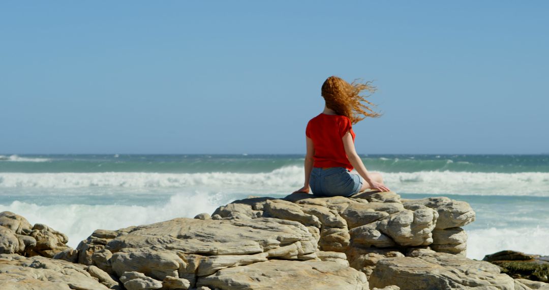 Woman sitting on rocky shore looking at ocean waves - Free Images, Stock Photos and Pictures on Pikwizard.com