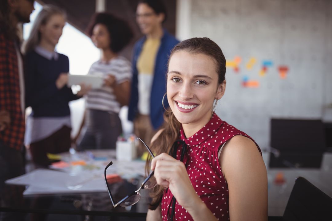 Smiling Businesswoman Holding Eyeglasses with Team in Background - Free Images, Stock Photos and Pictures on Pikwizard.com