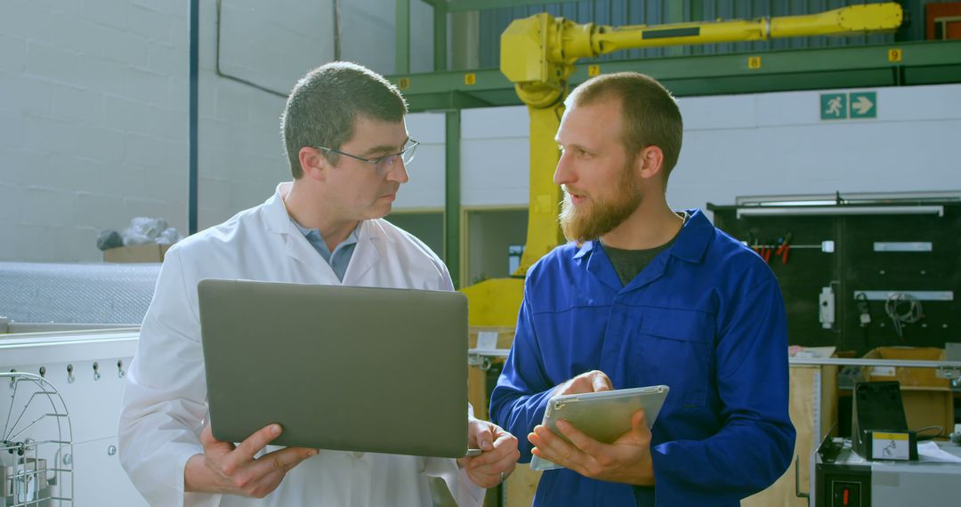 Two Engineers Discussing a Project with a Laptop and Tablet in a Factory - Free Images, Stock Photos and Pictures on Pikwizard.com