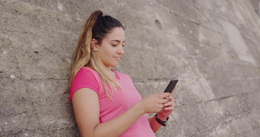 Young Woman in Pink T-Shirt Texting on Smartphone by Concrete Wall - Free Images, Stock Photos and Pictures on Pikwizard.com