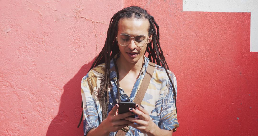 Young Man with Dreadlocks Using Smartphone Against Coral Wall - Free Images, Stock Photos and Pictures on Pikwizard.com