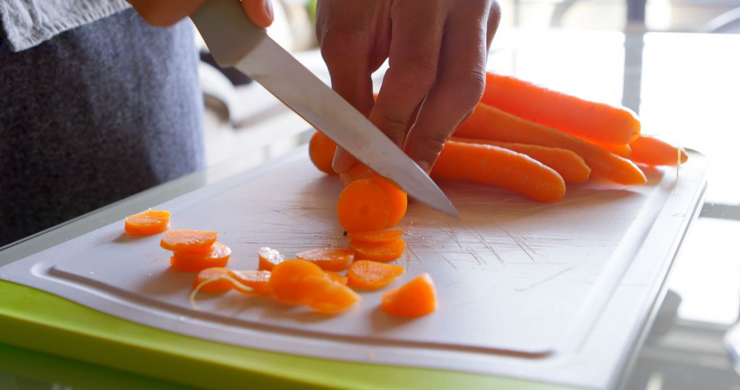 A person is slicing carrots on a white cutting board, with copy space - Free Images, Stock Photos and Pictures on Pikwizard.com