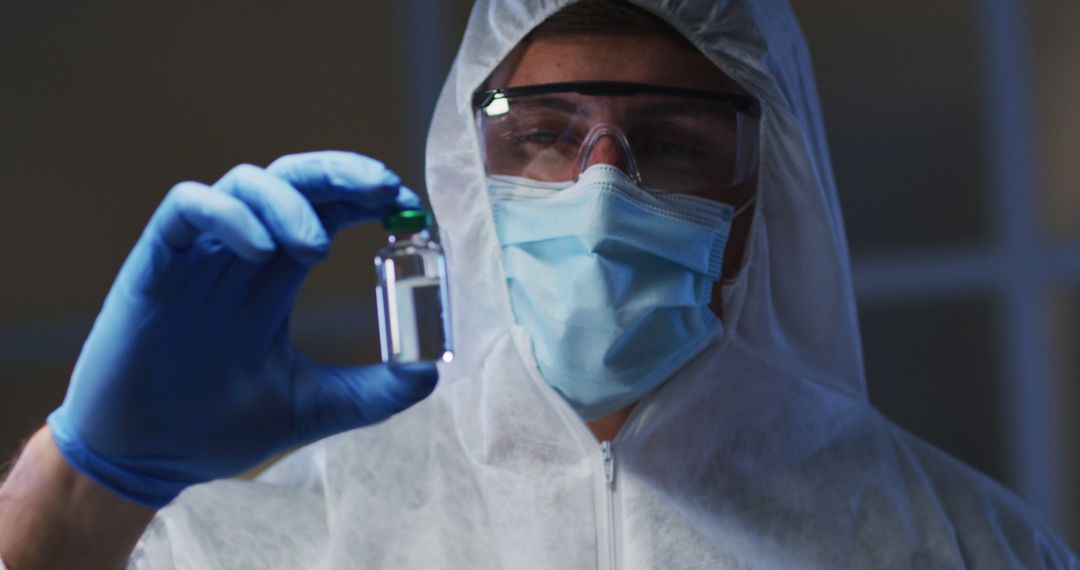 Healthcare worker in PPE holds a vaccine vial amid COVID-19 research efforts. - Free Images, Stock Photos and Pictures on Pikwizard.com