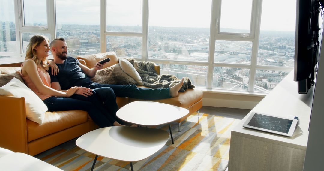 Couple Relaxing on Couch Watching TV in Modern Apartment with City View - Free Images, Stock Photos and Pictures on Pikwizard.com