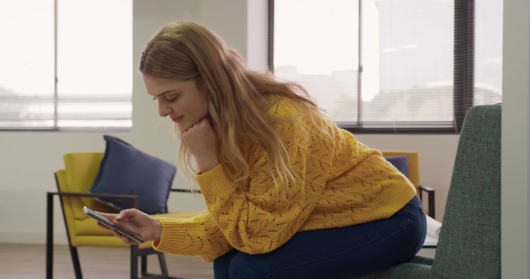 Young Woman in Yellow Sweater Checking Smartphone in Modern Office - Free Images, Stock Photos and Pictures on Pikwizard.com