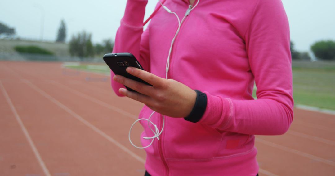 Female in Bright Pink Hoodie Using Smartphone on Outdoor Track - Free Images, Stock Photos and Pictures on Pikwizard.com