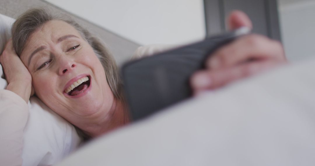 Smiling Senior Woman Laughing While Using Smartphone in Bed - Free Images, Stock Photos and Pictures on Pikwizard.com