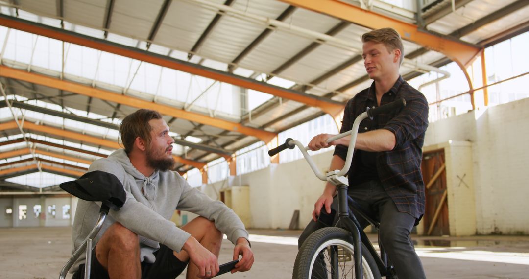 Two Friends Socializing in an Industrial Building with a Bicycle - Free Images, Stock Photos and Pictures on Pikwizard.com