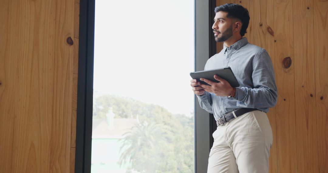 Professional Man Using Tablet by Large Window in Modern Office