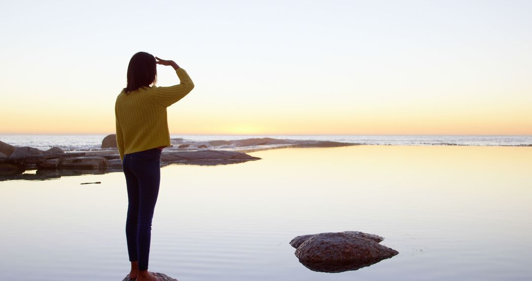 Woman Watching Sunset Over Calm Ocean from Rocky Shore - Free Images, Stock Photos and Pictures on Pikwizard.com