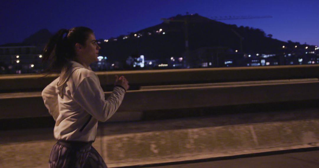 Young woman running on city bridge at night with hills in background - Free Images, Stock Photos and Pictures on Pikwizard.com