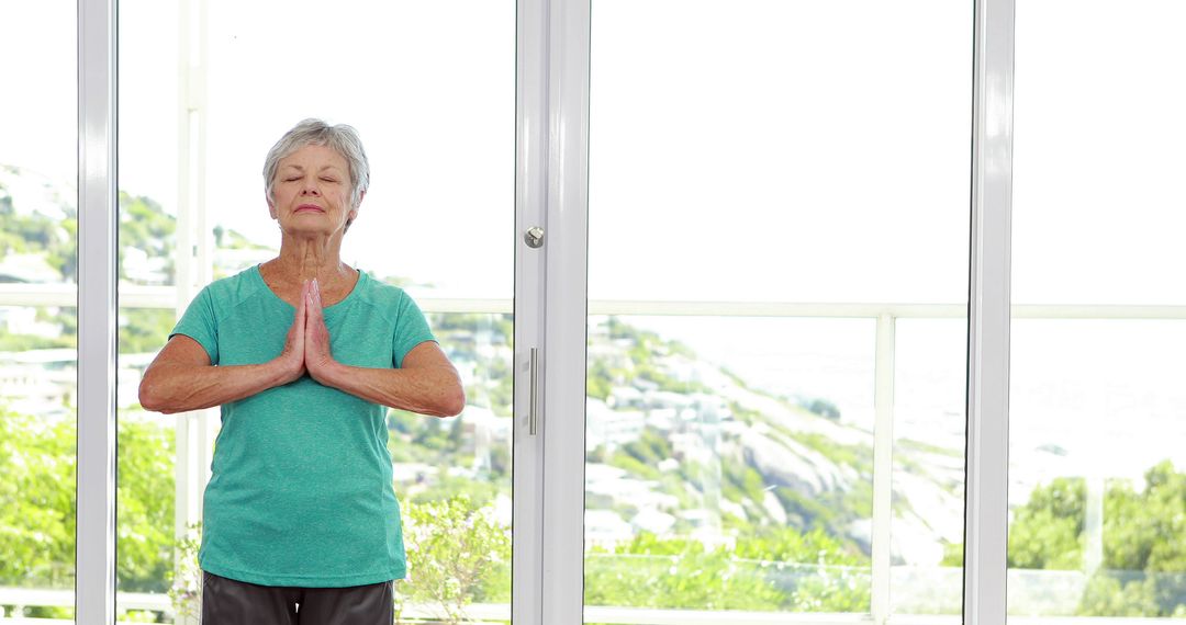 Senior Woman Meditating in Bright Room with Glass Wall - Free Images, Stock Photos and Pictures on Pikwizard.com