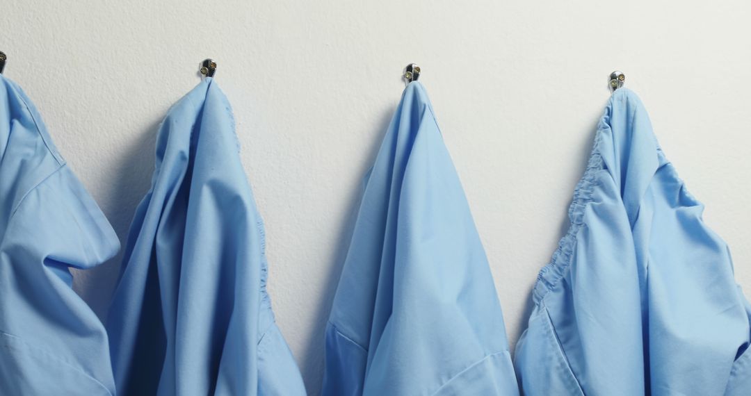 Blue medical scrubs are neatly hung on hooks against a white wall, with copy space - Free Images, Stock Photos and Pictures on Pikwizard.com