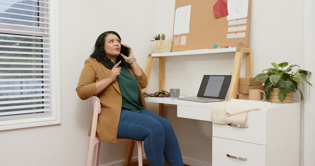 Mid adult woman talking on phone while working at bright minimalist home office desk