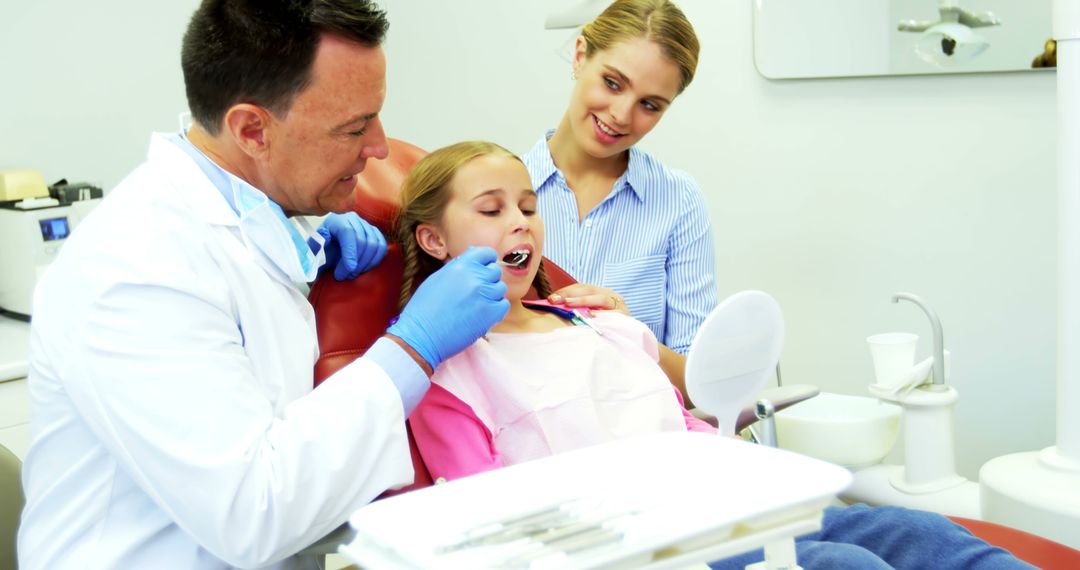 Friendly Dentist Treating Young Girl with Caring Mother Beside - Free Images, Stock Photos and Pictures on Pikwizard.com