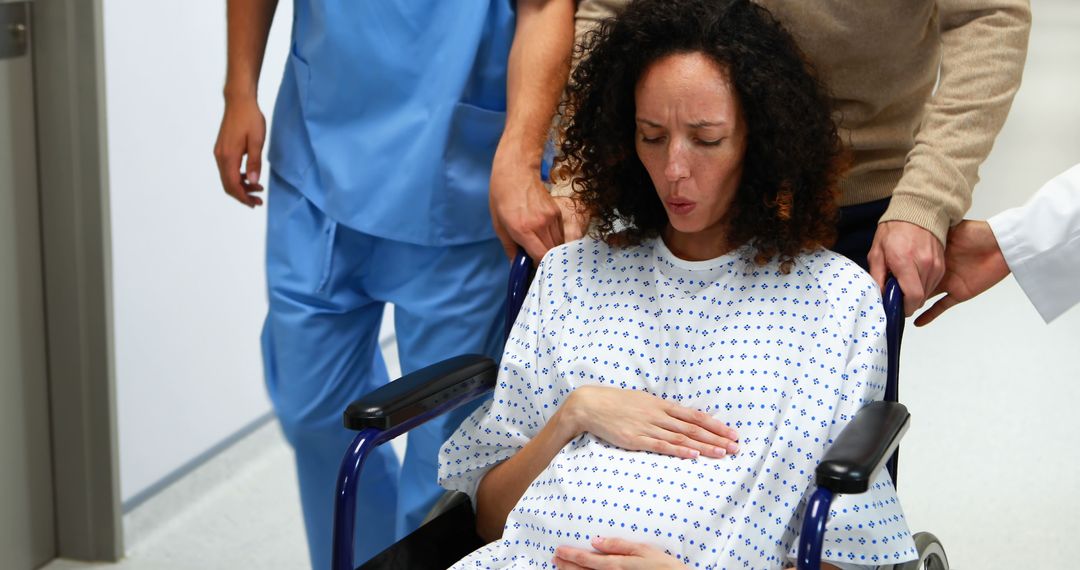 Pregnant woman in labor being pushed in wheelchair in hospital corridor - Free Images, Stock Photos and Pictures on Pikwizard.com