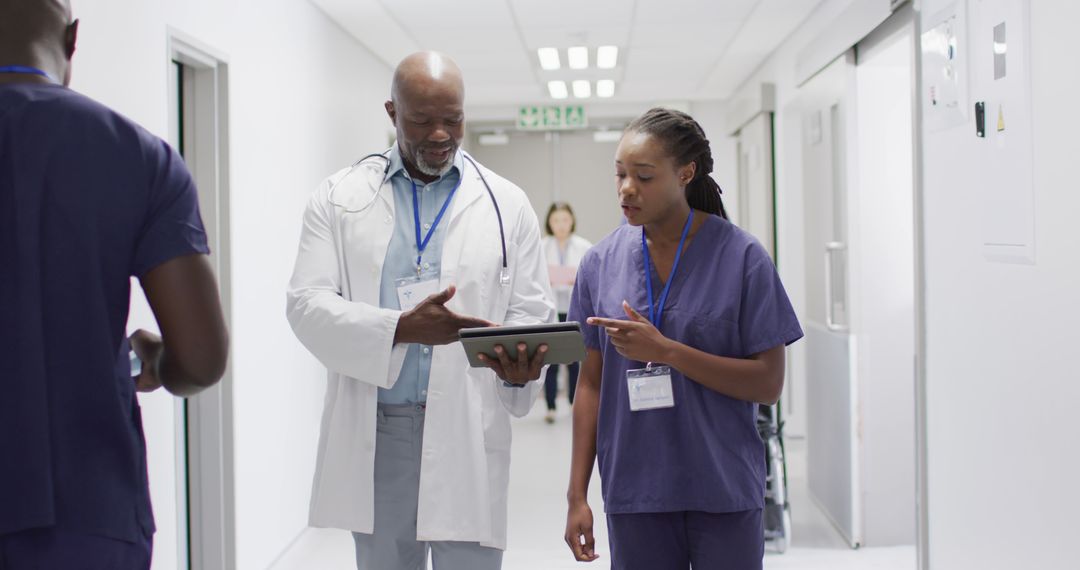 Doctors Discussing Patient Case on Digital Tablet in Hospital Corridor - Free Images, Stock Photos and Pictures on Pikwizard.com