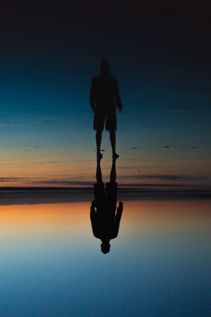 Silhouette of Man Reflecting on Calm Water During Dusk at Beach - Free Images, Stock Photos and Pictures on Pikwizard.com