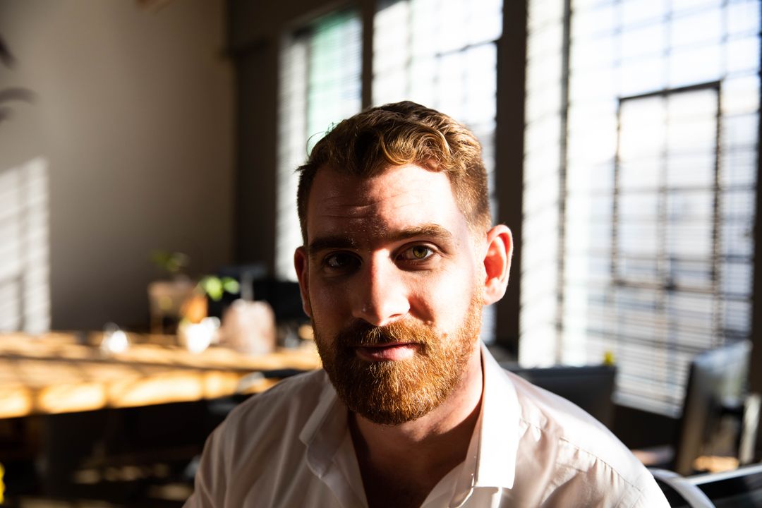 Reflective Man in Sunlit Workspace with Blinds