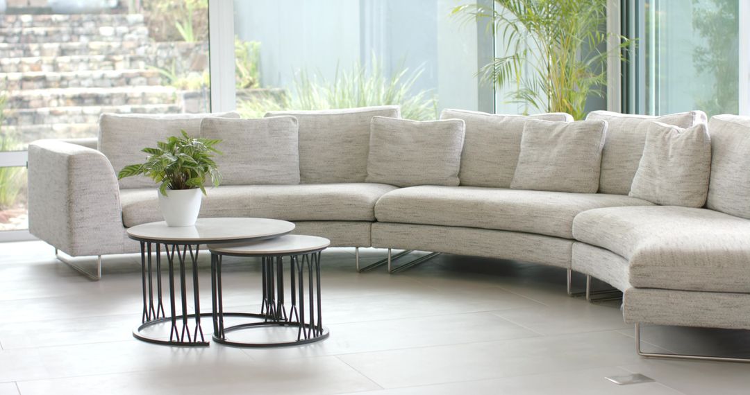 Light-Gray Curved Sectional Sofa with Nesting Tables and Plant in Modern Glass Lounge