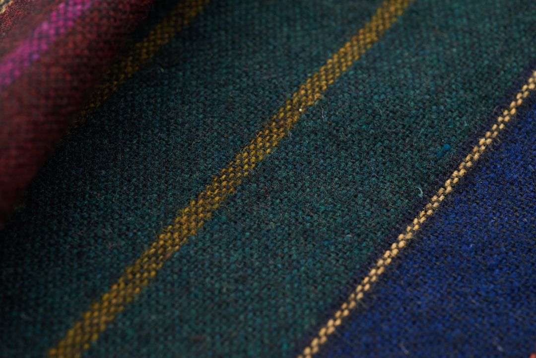 Close-up wool tweed fabric featuring diagonal yellow stripes on deep green and blue