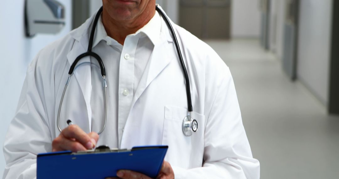 Caucasian Doctor Taking Notes in Hospital Hallway Wearing Stethoscope - Free Images, Stock Photos and Pictures on Pikwizard.com