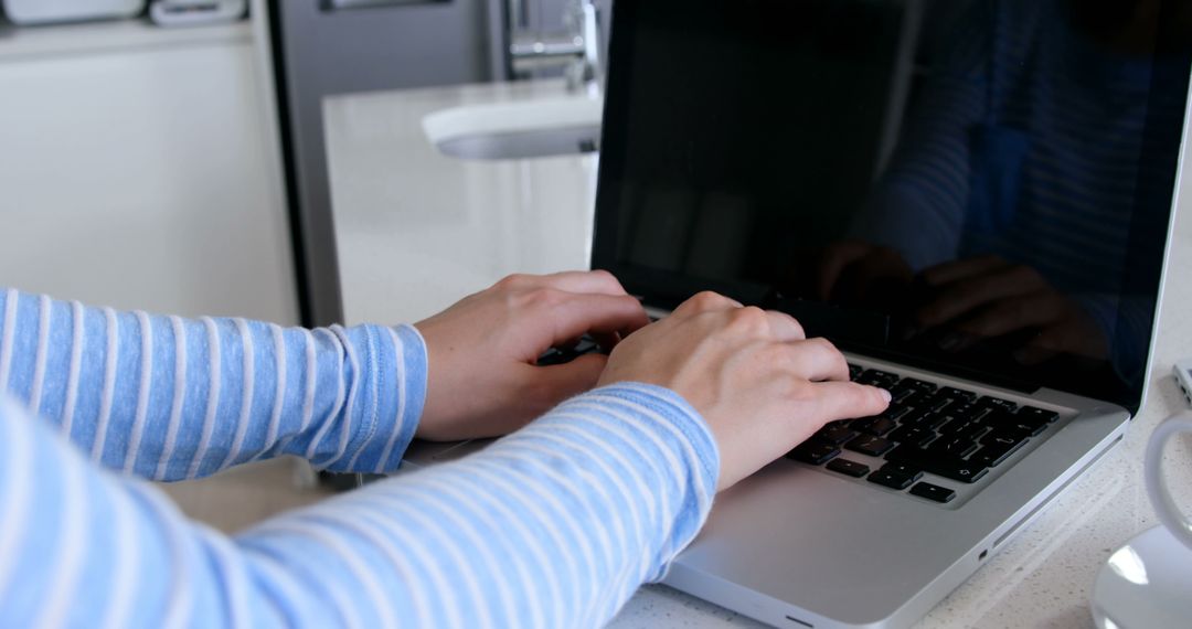 Person Typing on Laptop in Bright Kitchen with Blue Striped Top - Free Images, Stock Photos and Pictures on Pikwizard.com