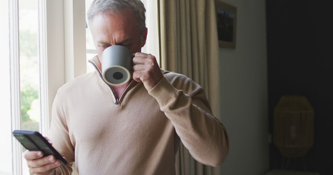 Middle-aged man drinking coffee while using smartphone at home - Free Images, Stock Photos and Pictures on Pikwizard.com